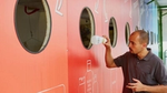 Mann wirft eine Plastikflasche in eine große bunte Recyclingstation.